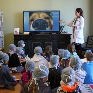 veterinarian presenting to a group of kids, with a picture of a dog's nose on the tv screen